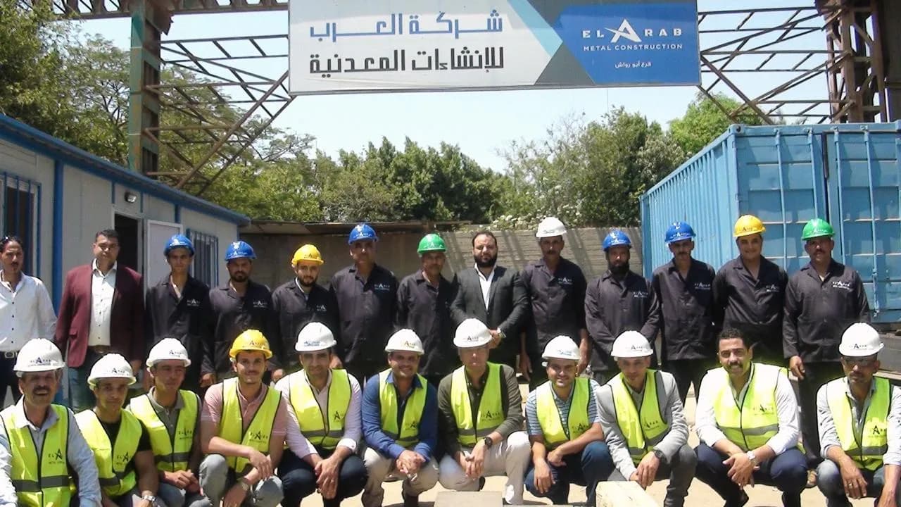 فنيان من شركة العرب يقومان بتجهيز عارضة معدنية داخل ورشة التصنيع مع تطاير الشرر